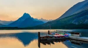 Peaceful sunset over a mountain lake with canoes lined up on a wooden dock, reflecting the tranquil mood.